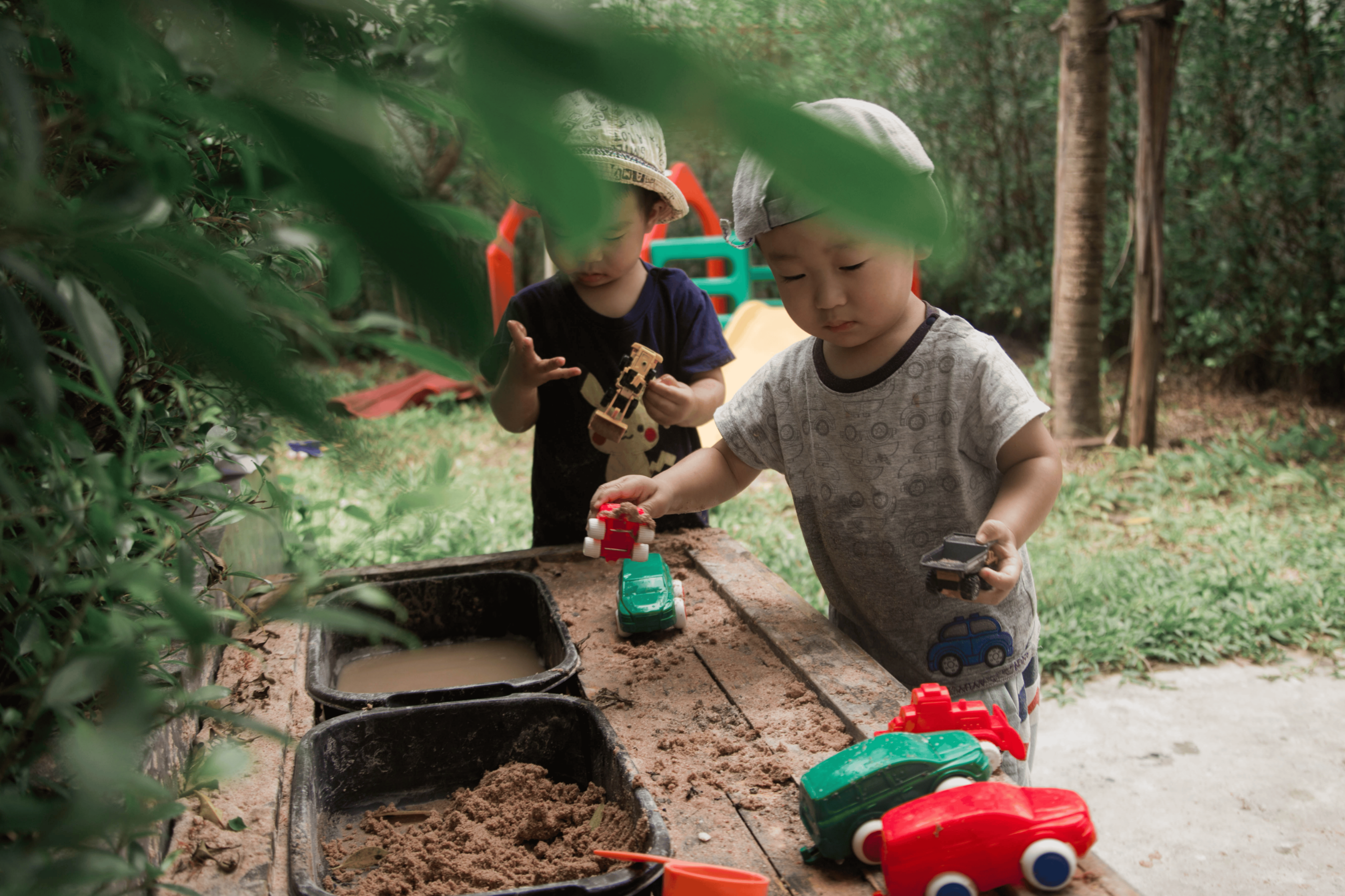 Children playing with toy cars near a sand pit outdoors